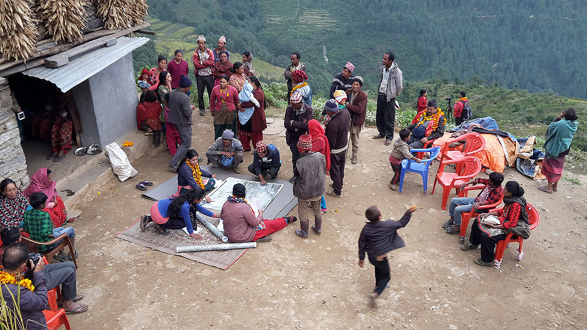 Volunteer community surveyor Shristi Paudel (sitting cross legged next to the map with yellow and orange flowers around her neck) working with a community in Nepal 