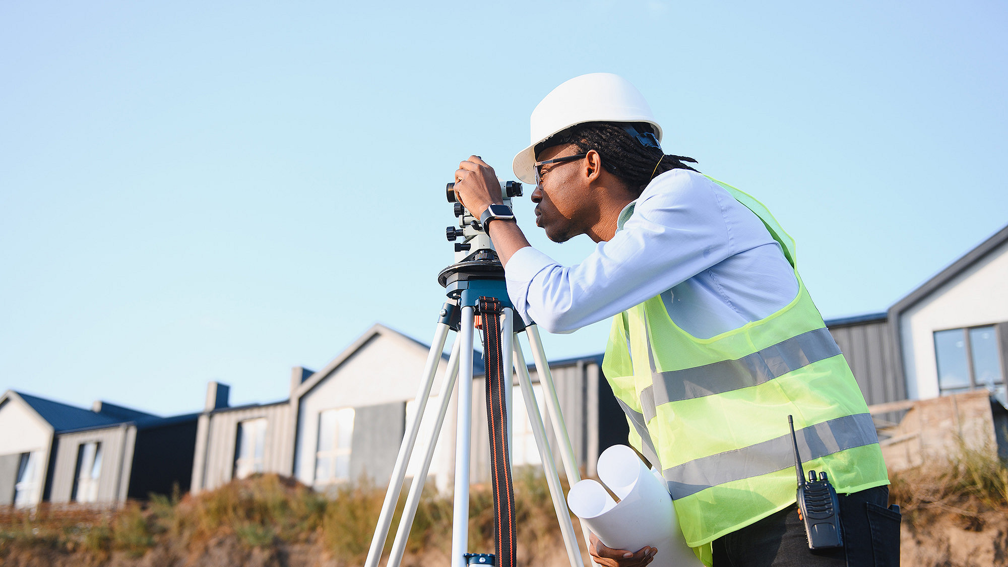 Colour photograph of a surveyor wearing a hard hat and using a theodolite.