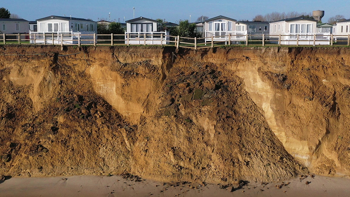 Dwellings at the edge of cliff showing erosion down to beach