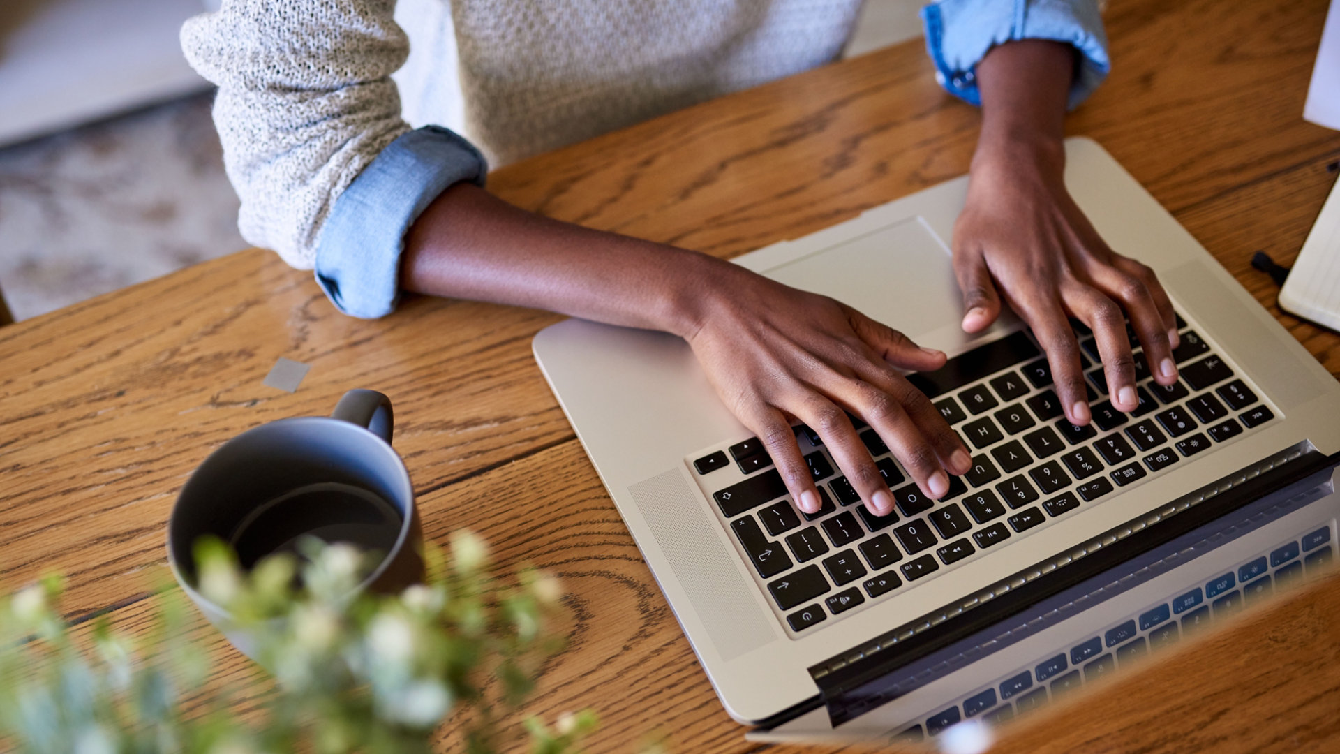 A young woman sat at a wooden table using a laptop