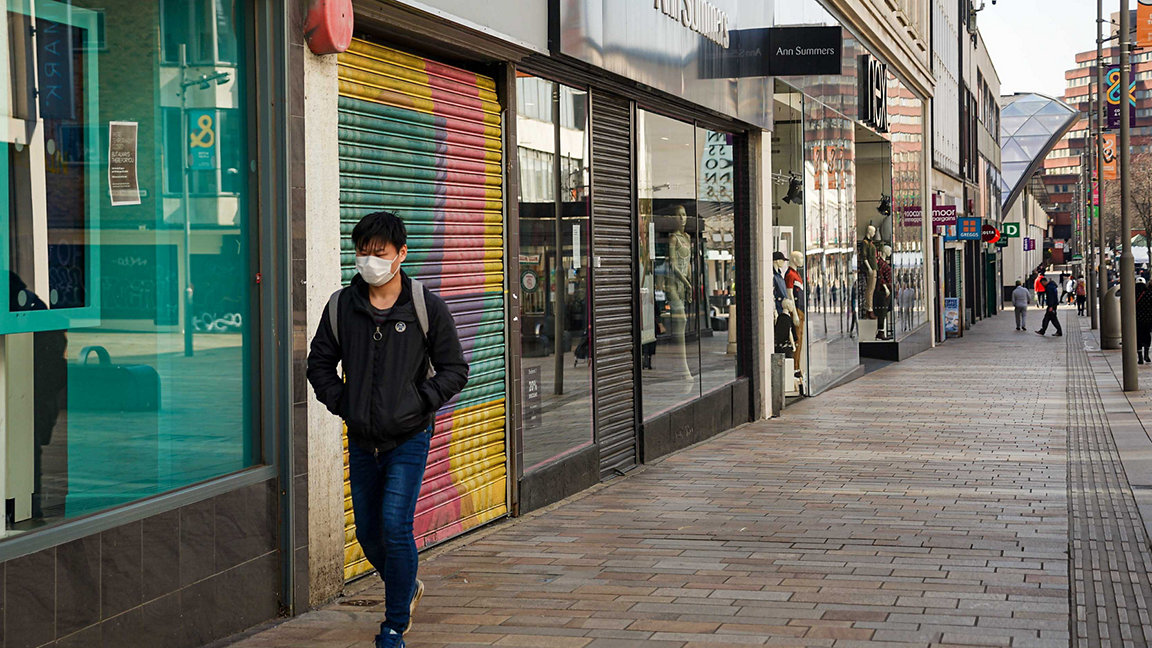 UK high street with shuttered shops during COVID lockdown, lone male pedestrian wearing a face mask