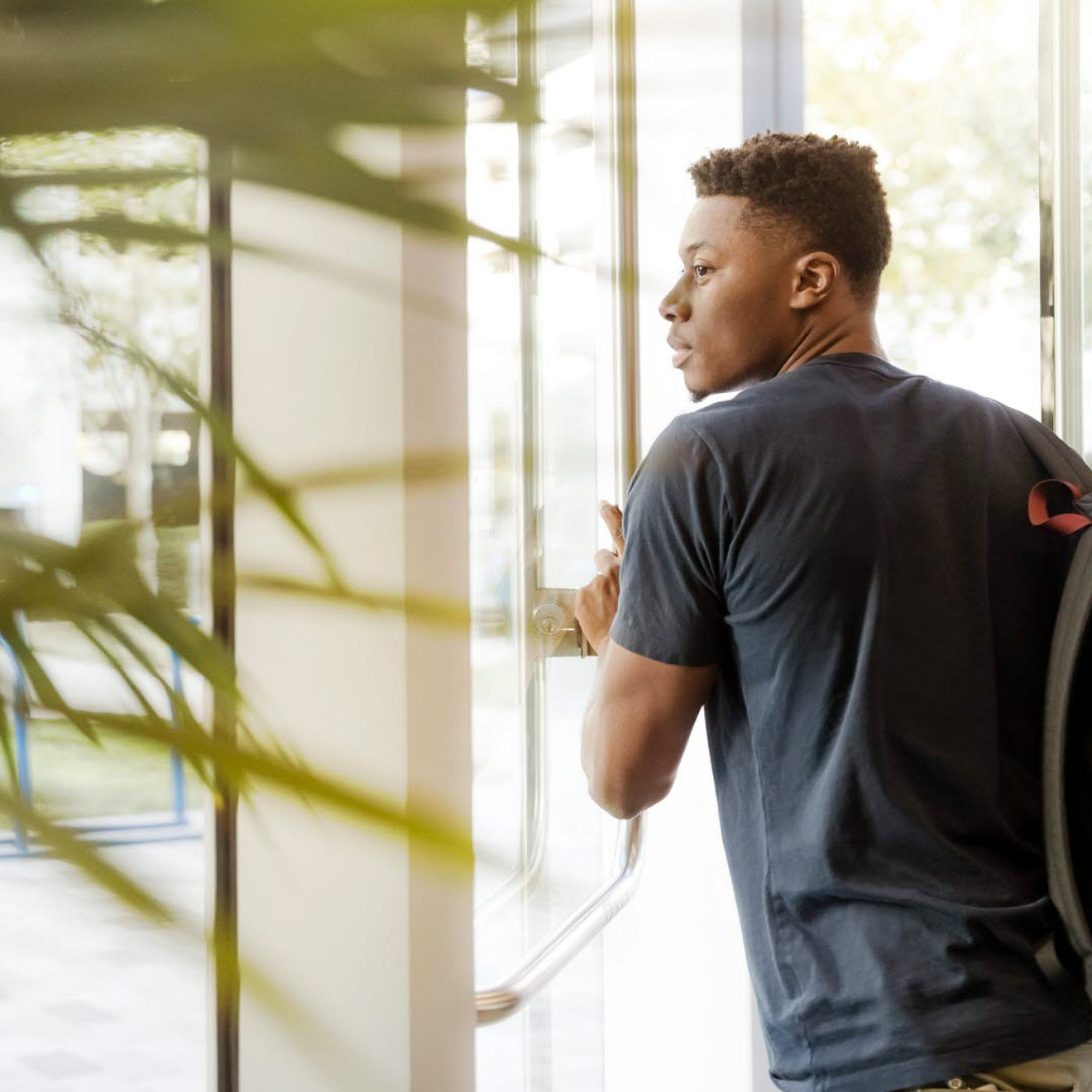 A student in a university wearing a backpack. They are walking through a glass doorway.