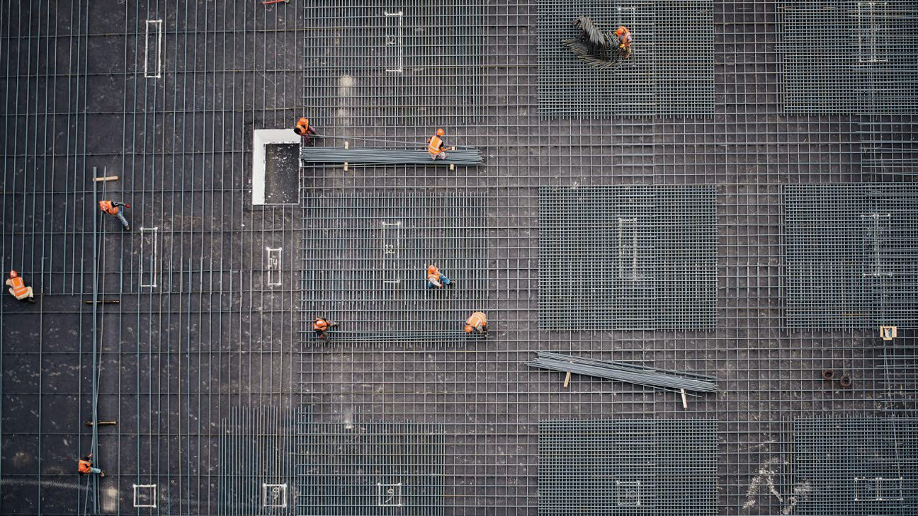 Structural metal framework being constructed by a workforce as viewed from above