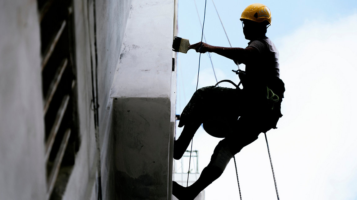 Painter hanging from a harness painting the exterior wall of a commercial building