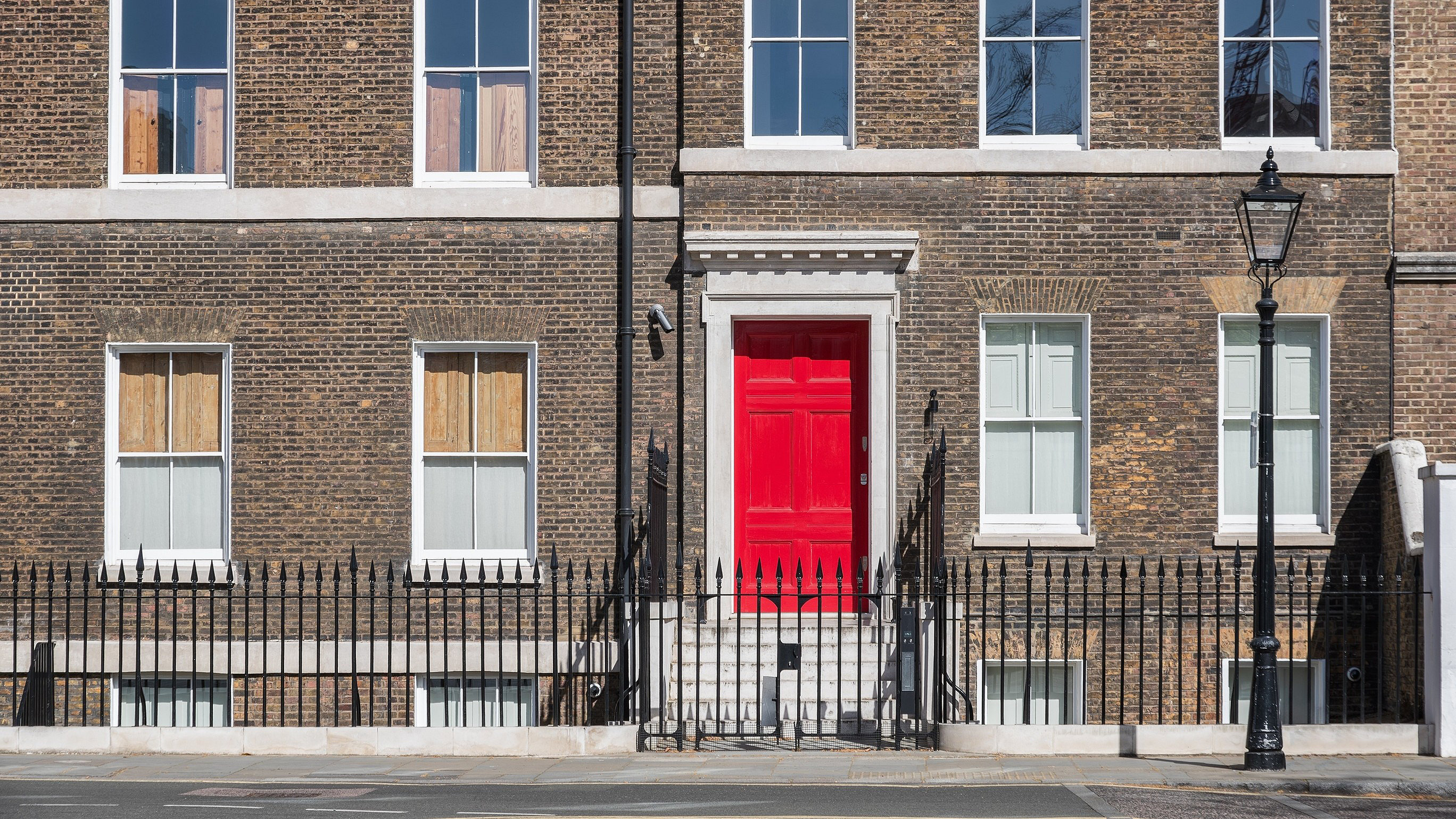 Facade of a brick building with a symmetrical arrangement of sash windows and a red door in London, England