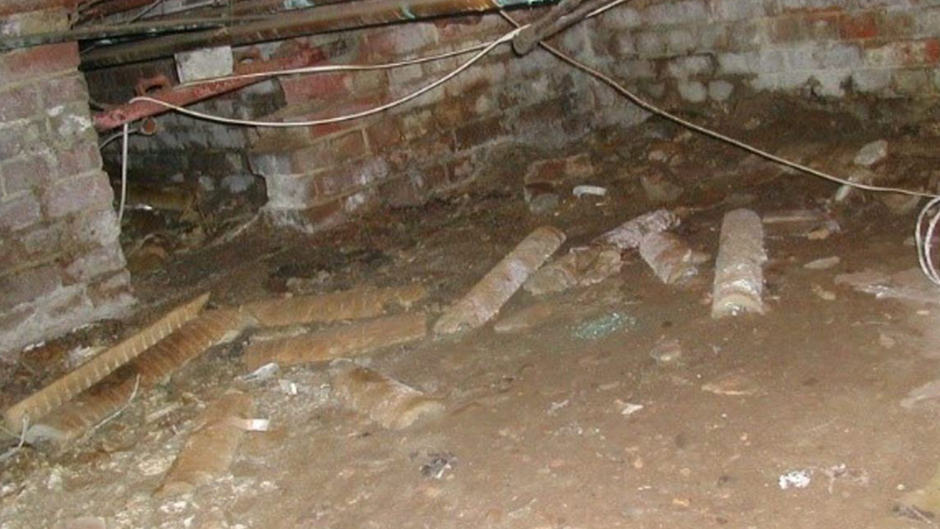 Underfloor crawlspace with l oose sections of asbestos insulation on the floor