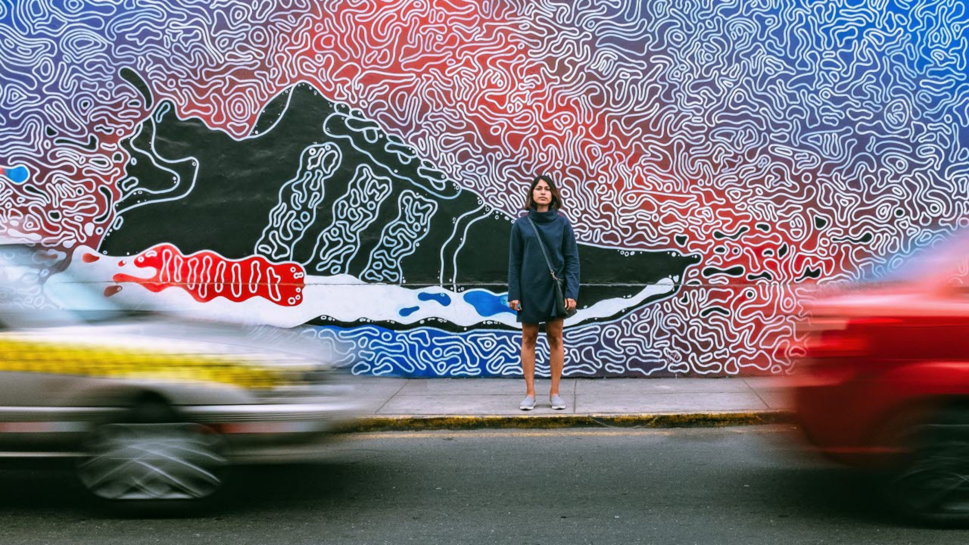 Woman standing in front of wall art of footwear whilst cars pass by