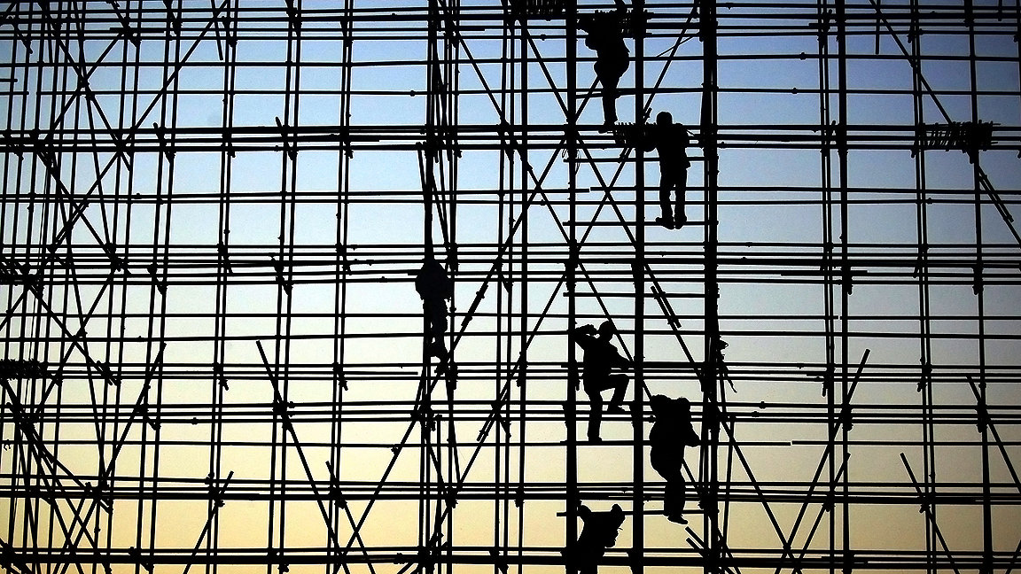 Photo of workers climbing up scaffolding on a gradient sky background