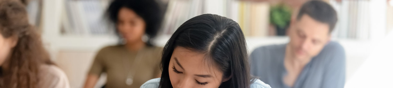 Focused millennial Asian female student sit in shared coworking space studying with handbook writing do homework, concentrated teen girl make notes in workbook prepare for test or exam in library; Shutterstock ID 1401389816; purchase_order: N/A; job: ; client: RICS_PP; other: 