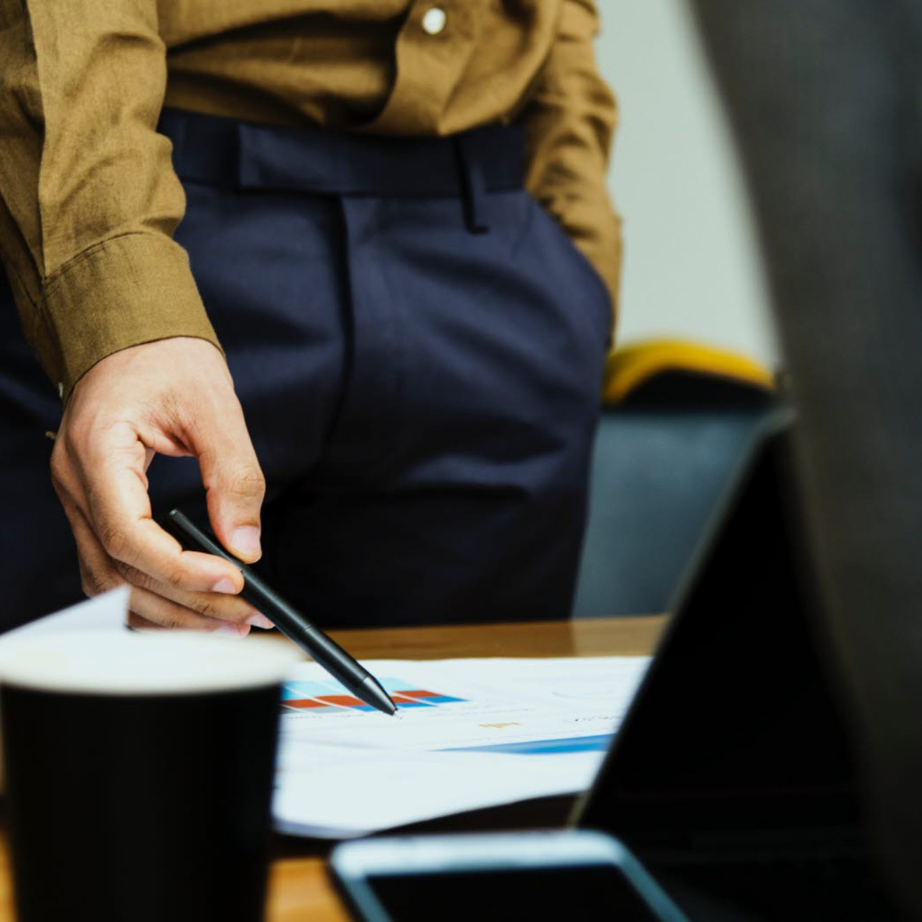 A close up of a man pointing at paperwork on a desk using a pen.