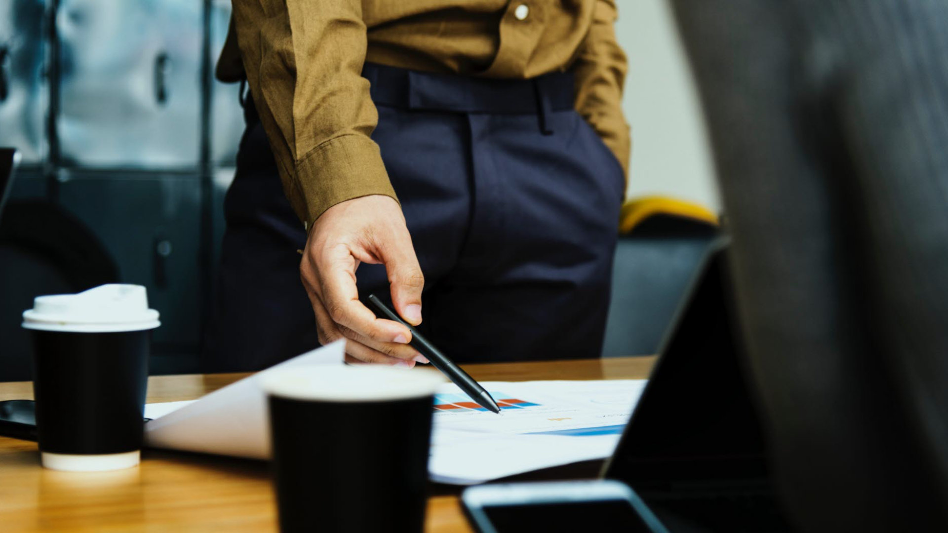 A close up of a man pointing at paperwork on a desk using a pen.