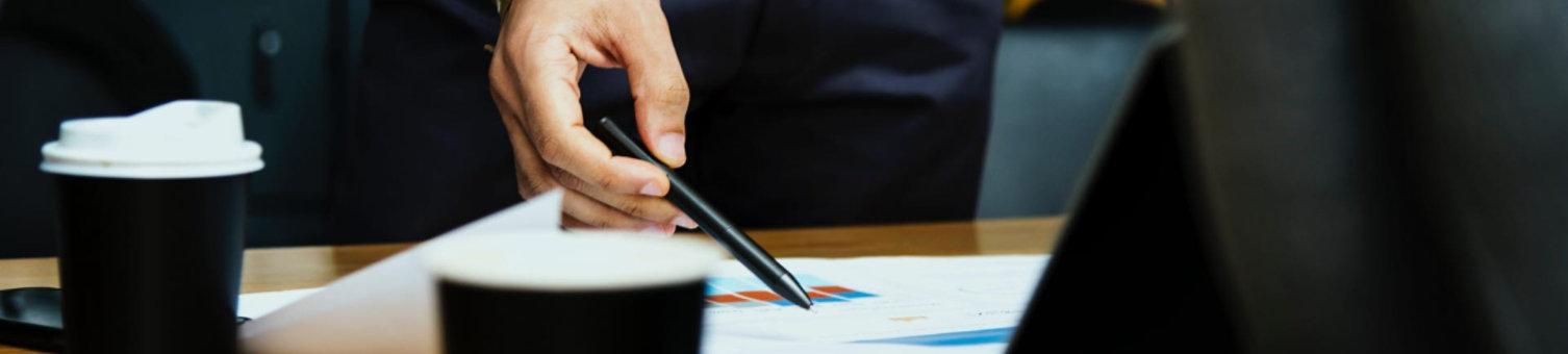 A close up of a man pointing at paperwork on a desk using a pen.