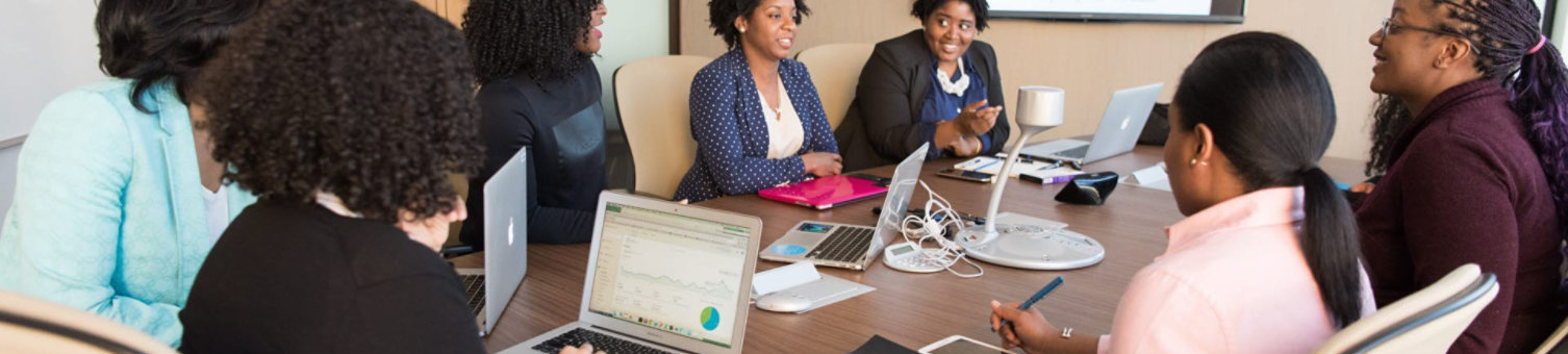Business women sat around a meeting table with their laptops open