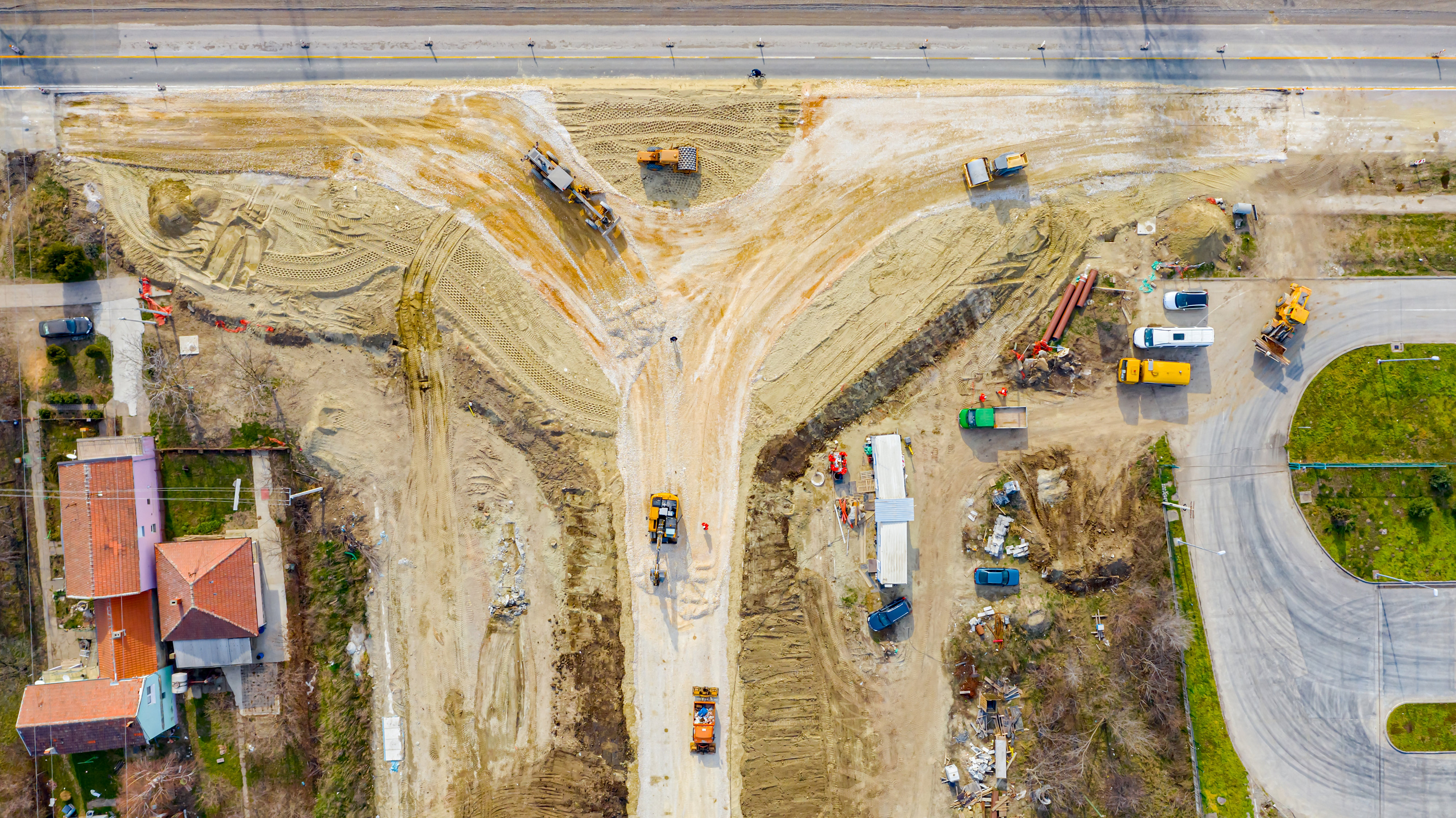 Above top view, overhead on circular road, roundabout under construction, crew of workers at building site working on road foundation with heavy machinery.