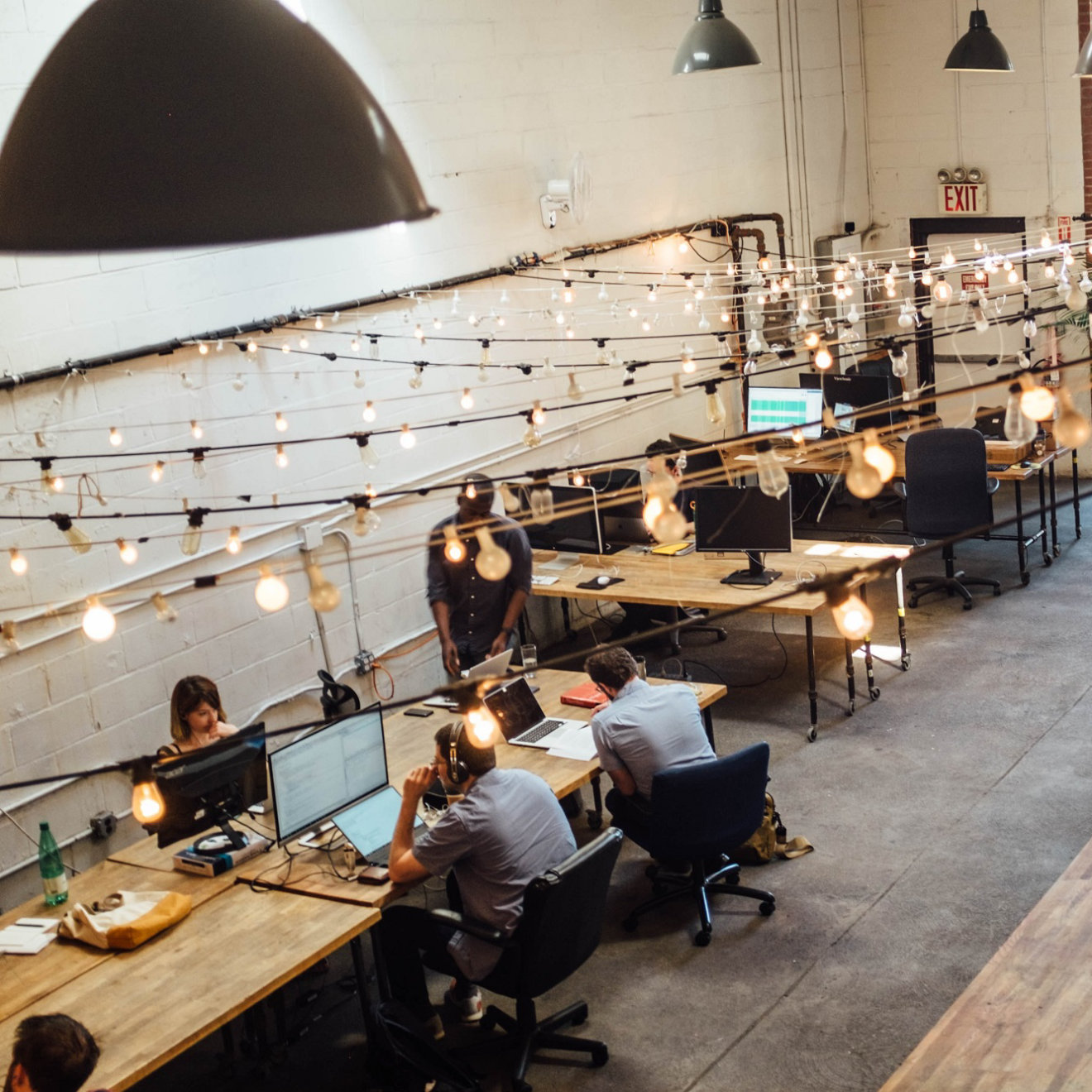 A photo of a modern office environment with wooden desks. Strings of lights run overhead.