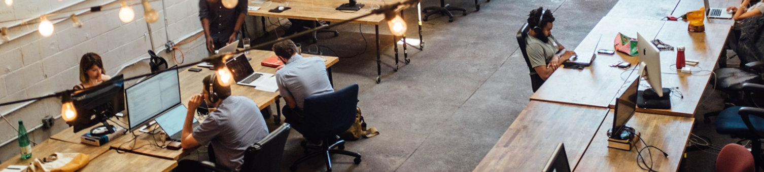 A photo of a modern office environment with wooden desks. Strings of lights run overhead.