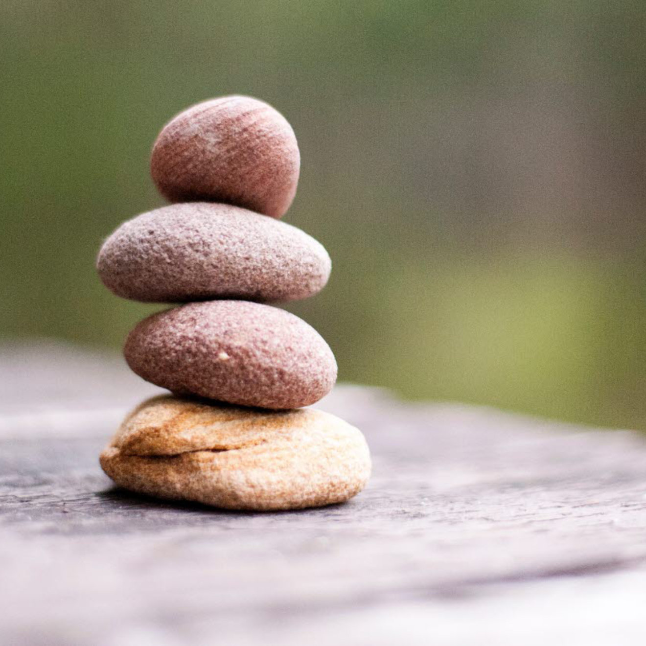 A stack of four pebbles on a wooden bench outdoors