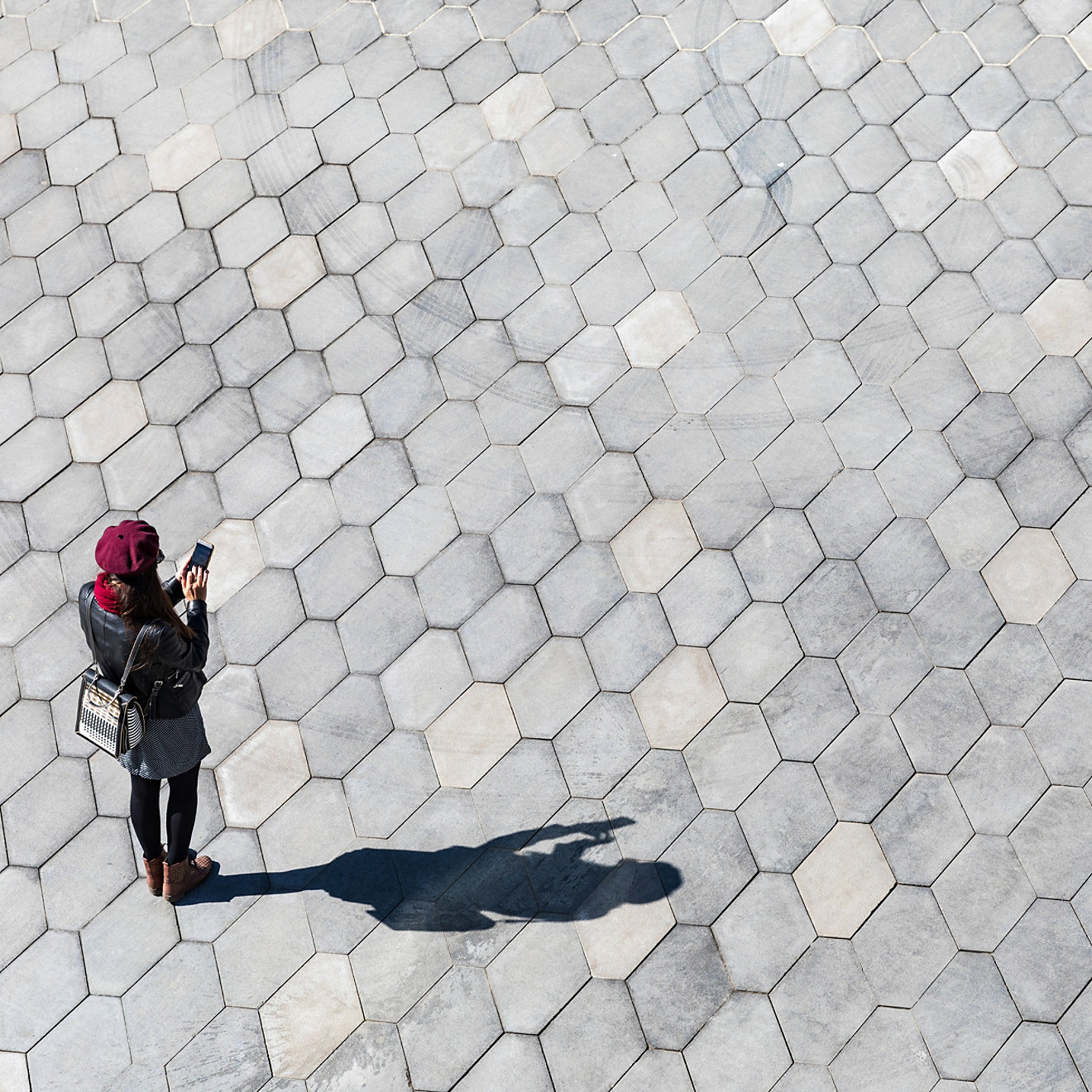 Woman typing on the phone, shadow and empty space. Minimal image, top view of a girl with a smartphone, and her shadow on the pavement. Technology concept, blank space to add text.