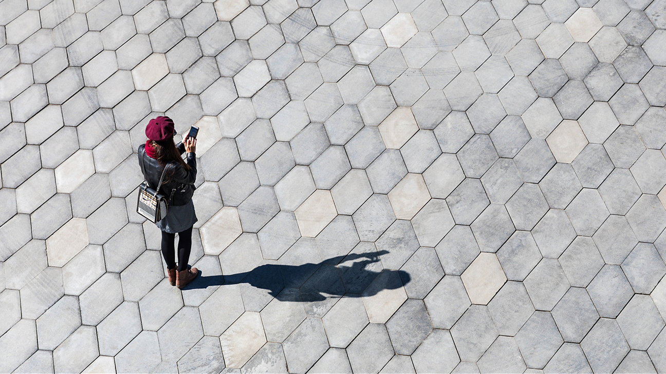 A woman on her phone walking across a paved area