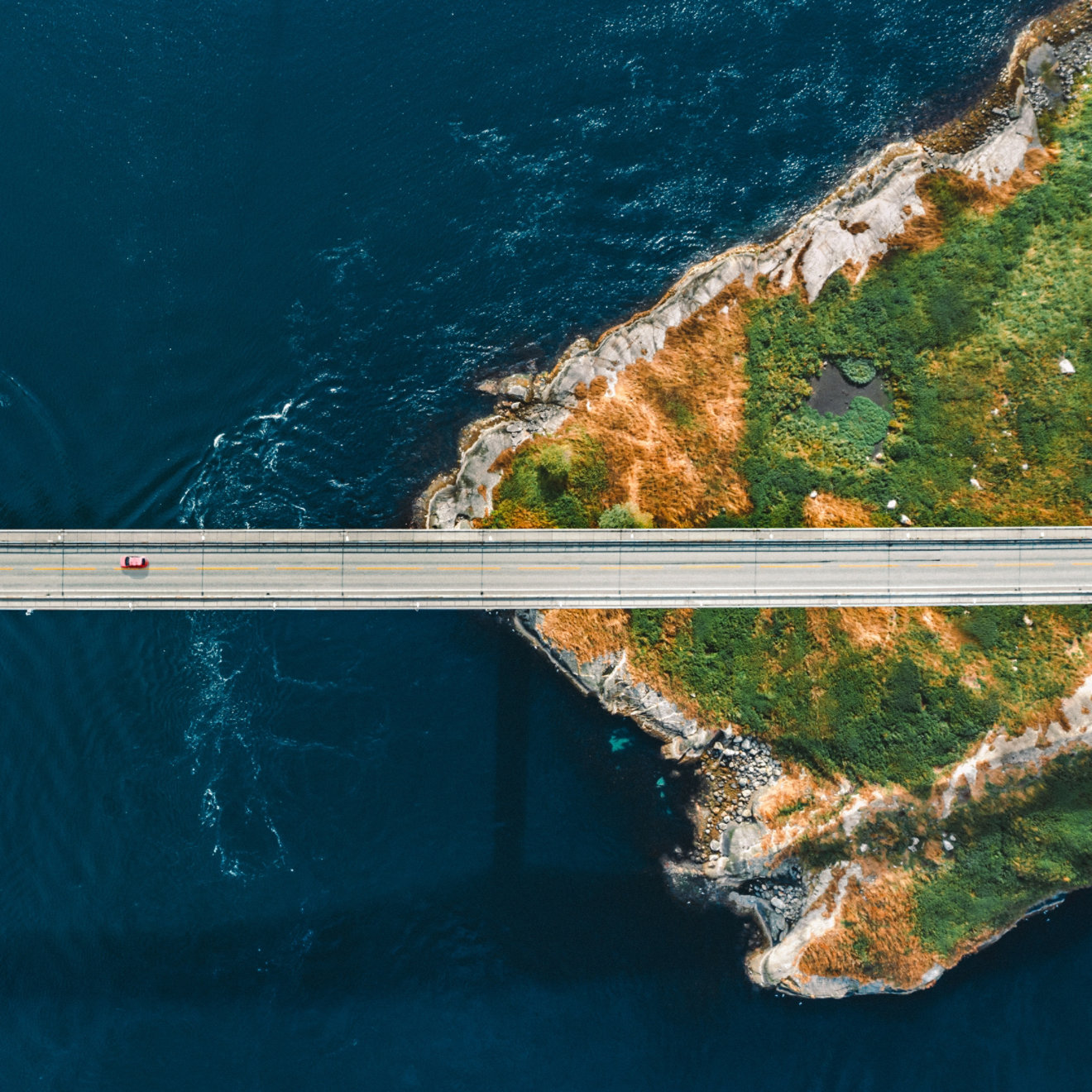 A car traveling along a narrow bridge over a stretch of water