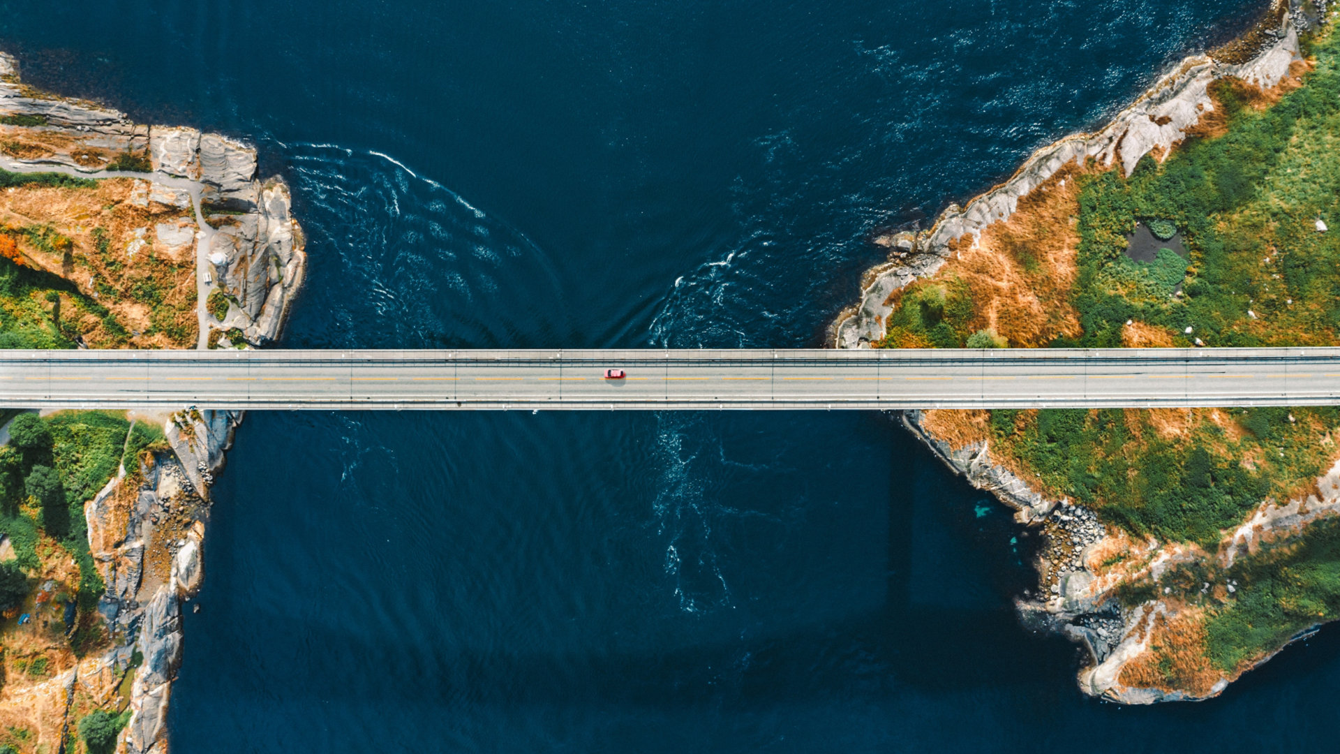 A car traveling along a narrow bridge over a stretch of water