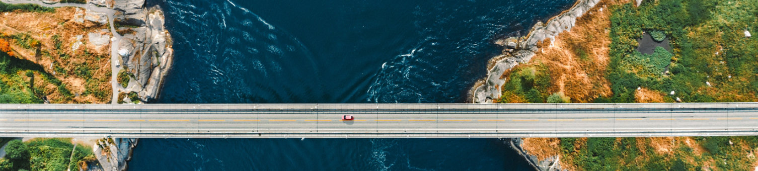 A car traveling along a narrow bridge over a stretch of water