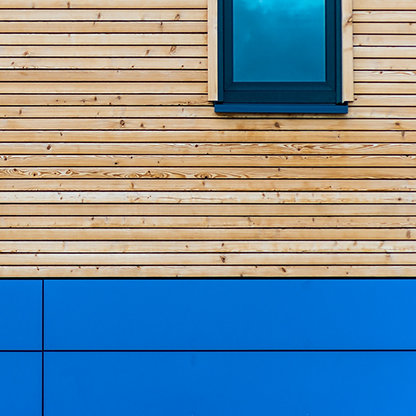 The side of a building showing wooden cladding and bright blue reflections on the windows