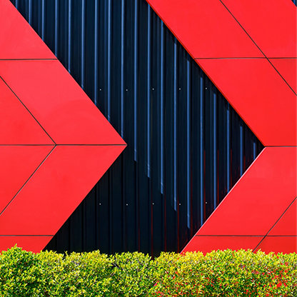 Front view of red arrows pattern on black corrugated metal wall behind green bush fence in exterior architecture decorations design concept; Shutterstock ID 1982992589; purchase_order: -; job: -; client: -; other: -