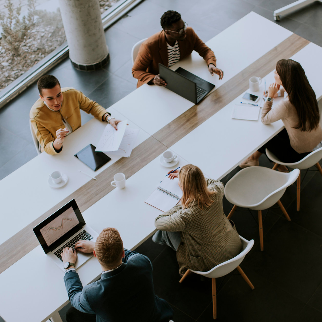 An overhead view of people working and talking at a long desk in an office environment