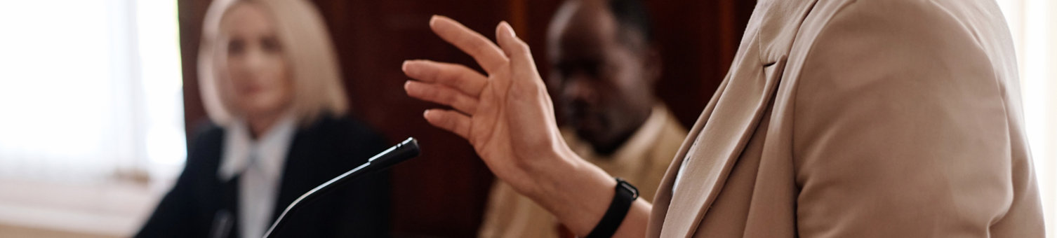 Cropped shot of young female witness in beige blazer standing by tribune; Shutterstock ID 2378803167; purchase_order: N/A; job: RICS Mediation, Expert Witness & DRS Imagery; client: RICS_PP; other: 
