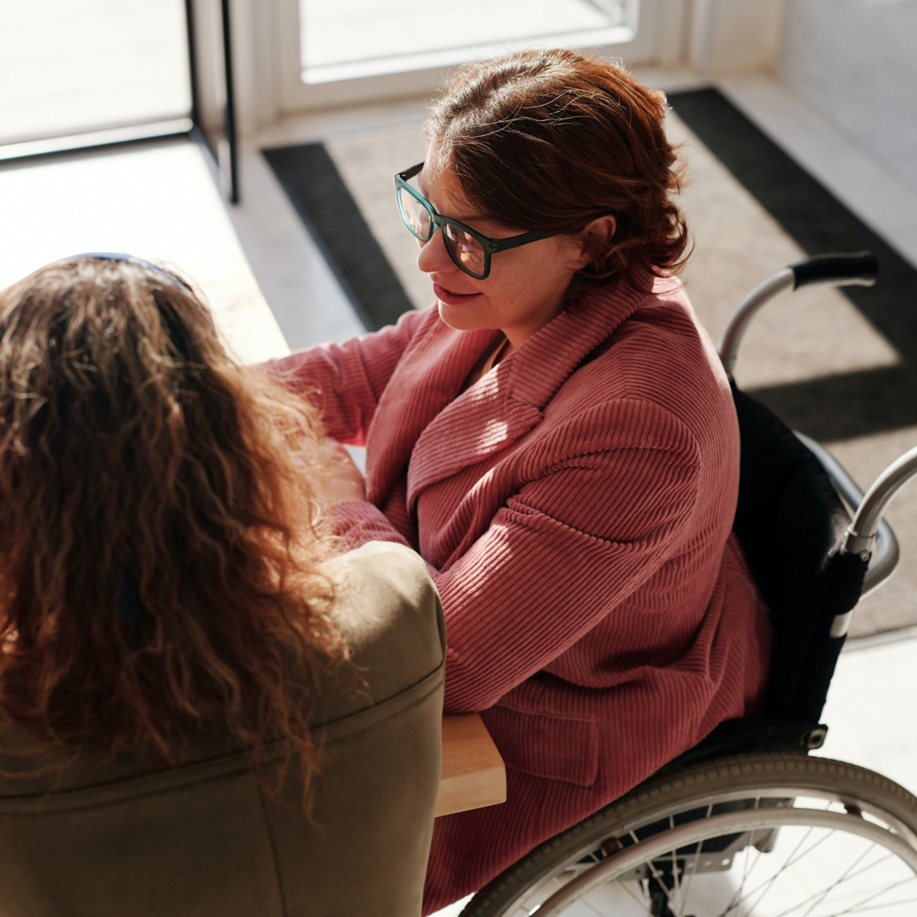 Two business people seated at a desk having a discussion. One is a wheelchair user.