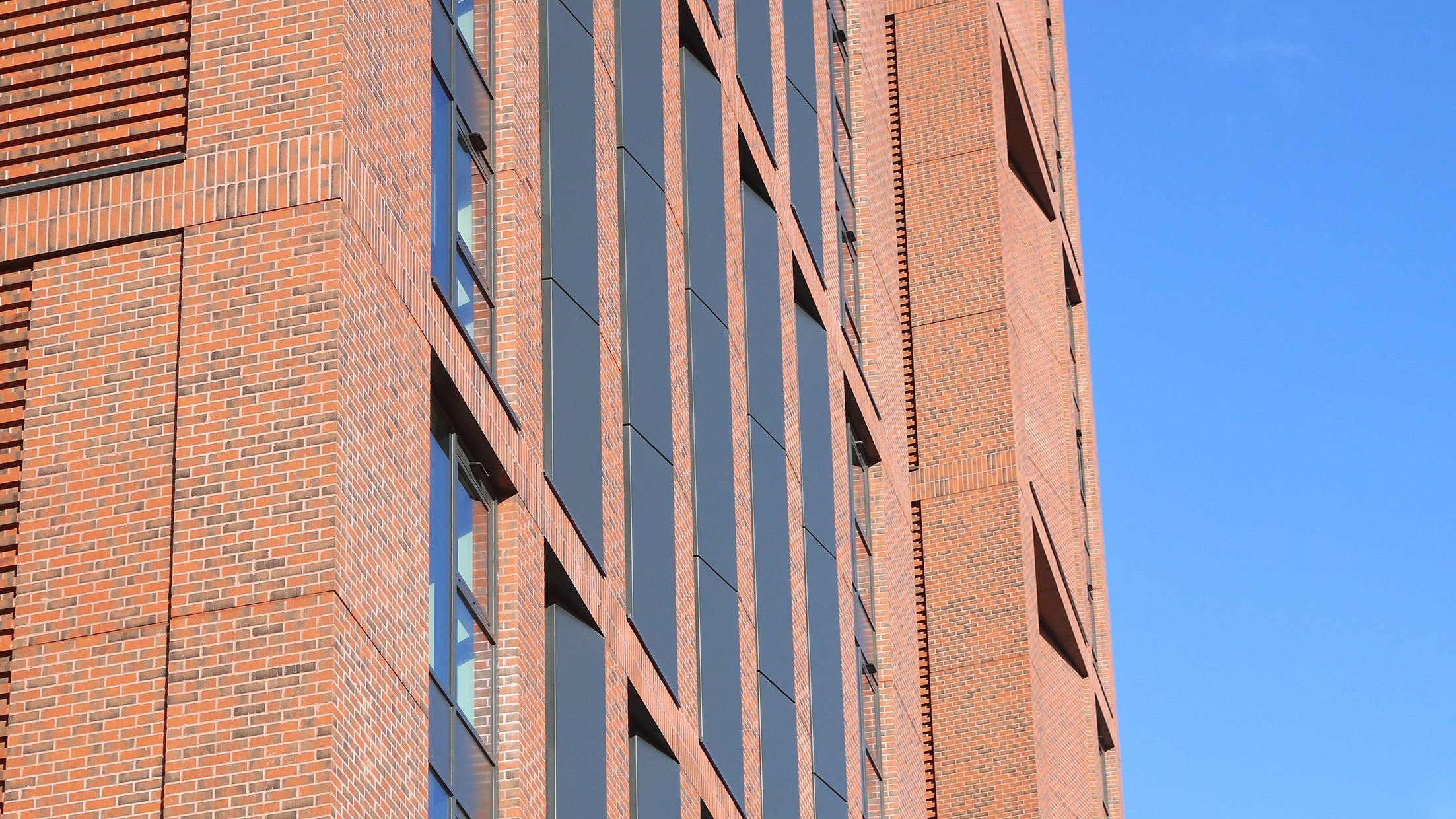 Close-up view of a red brick student accommodation building with section of blue sky