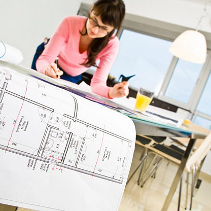 A woman at a drafting desk looking at blueprints