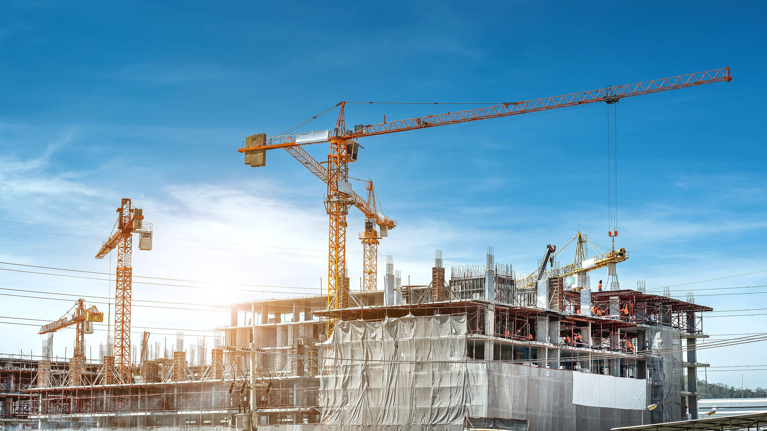 cranes working on top of a building in process of being construction against blue sky